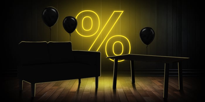  Svart sofa og trebord med svarte ballonger foran et lyst gult prosenttegn på et mørkt tregulv.