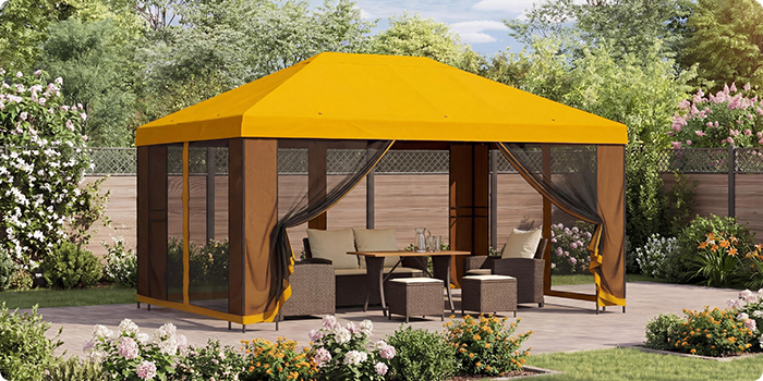 Gul hagepaviljong med nettinggardiner som dekker en sittegruppe med bord på en terrasse, omgitt av blomstrende planter i en solrik hage.